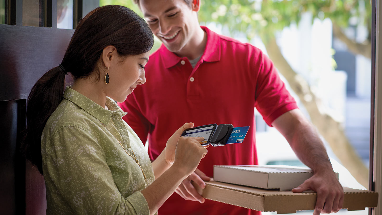 A pizza delivery person holding two pizza boxes as the customer is making a mobile payment.